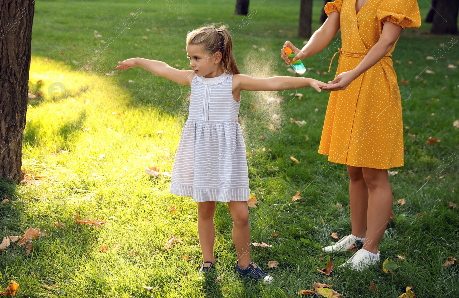 Photo of Mother applying insect repellent onto girl's hand in park