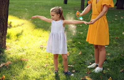 Mother applying insect repellent onto girl's hand in park