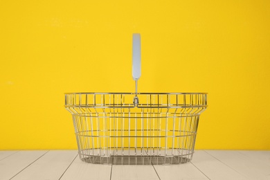 Photo of Empty metal shopping basket on white wooden table against yellow background