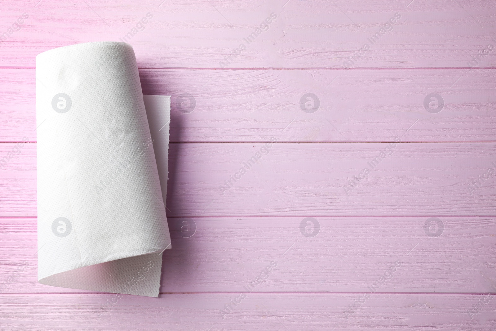 Photo of Roll of paper towel on pink wooden table, top view. Space for text