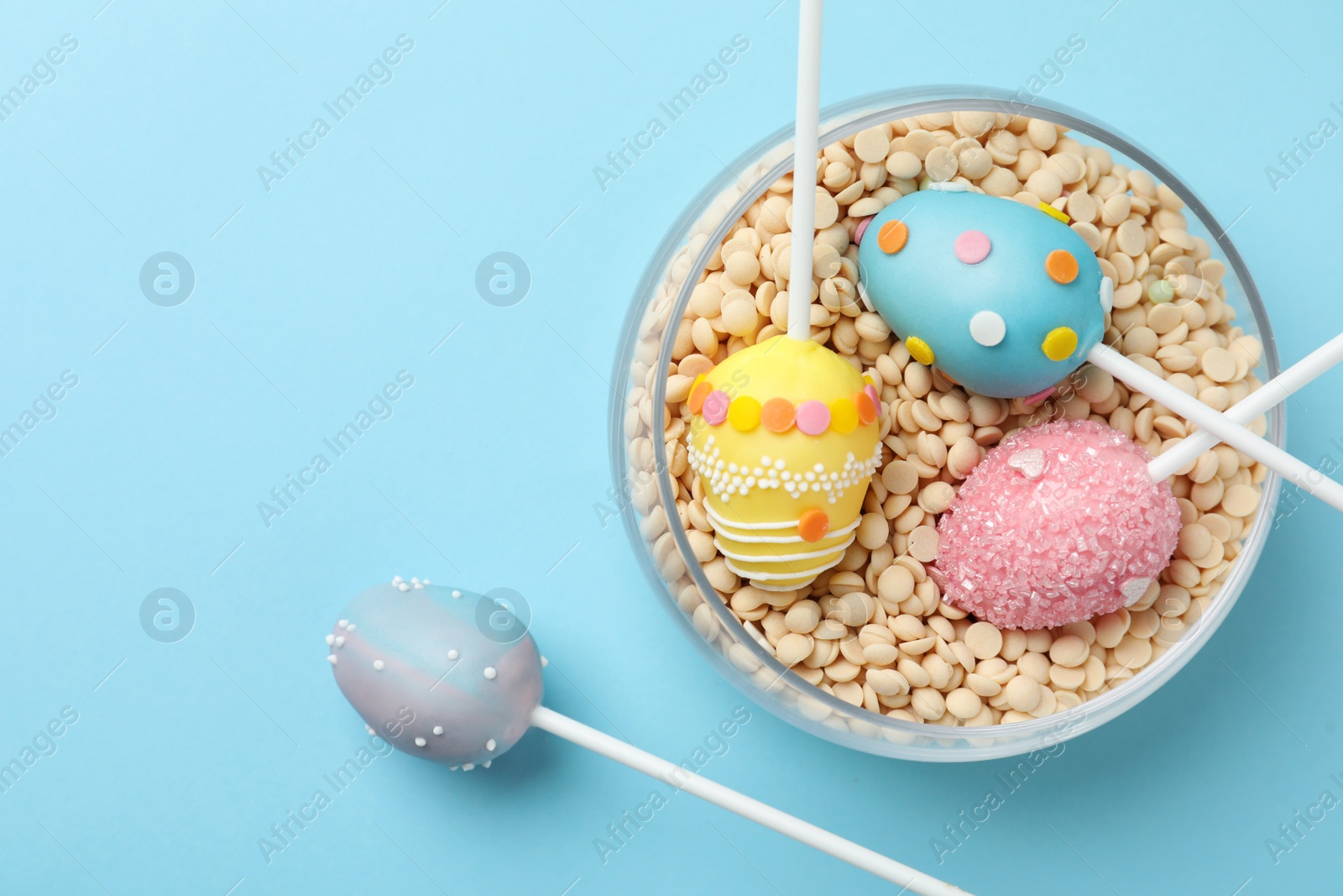 Photo of Egg shaped cake pops for Easter celebration on light blue background, flat lay