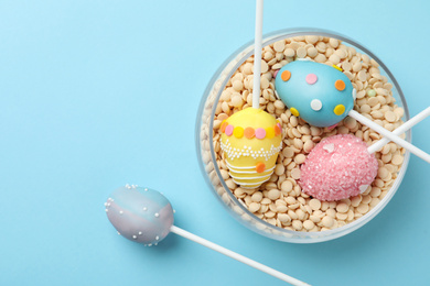 Egg shaped cake pops for Easter celebration on light blue background, flat lay