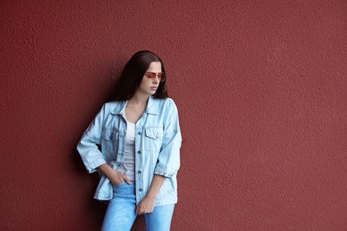 Young hipster woman in stylish jeans and jacket posing near color wall