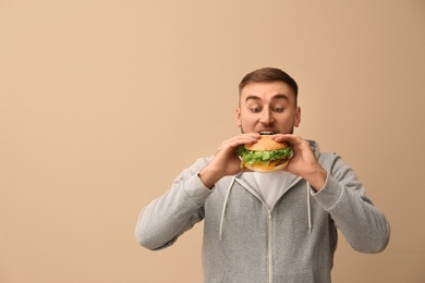 Young man eating tasty burger on color background. Space for text