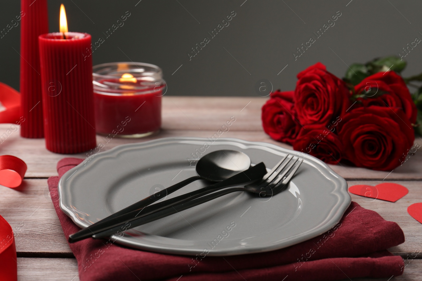 Photo of Romantic place setting with red roses and candles on wooden table. St. Valentine's day dinner