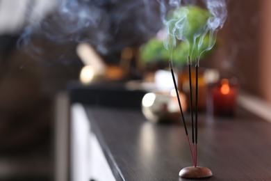 Photo of Incense sticks smoldering on wooden chest of drawers in room. Space for text