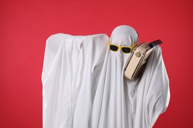 Person in ghost costume and sunglasses using retro radio receiver on red background