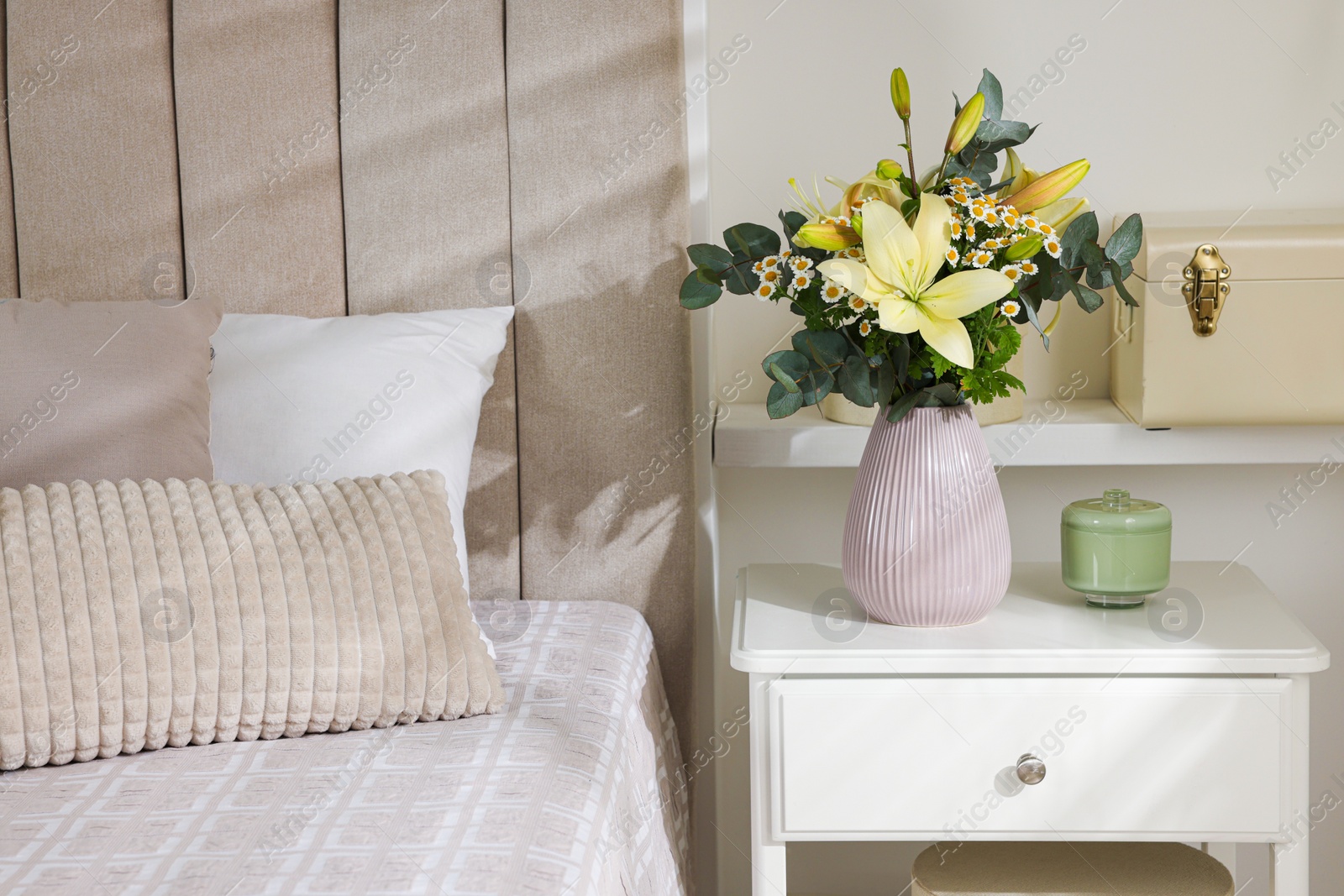 Photo of Stylish vase with flowers and decor on bedside table indoors. Bedroom interior elements