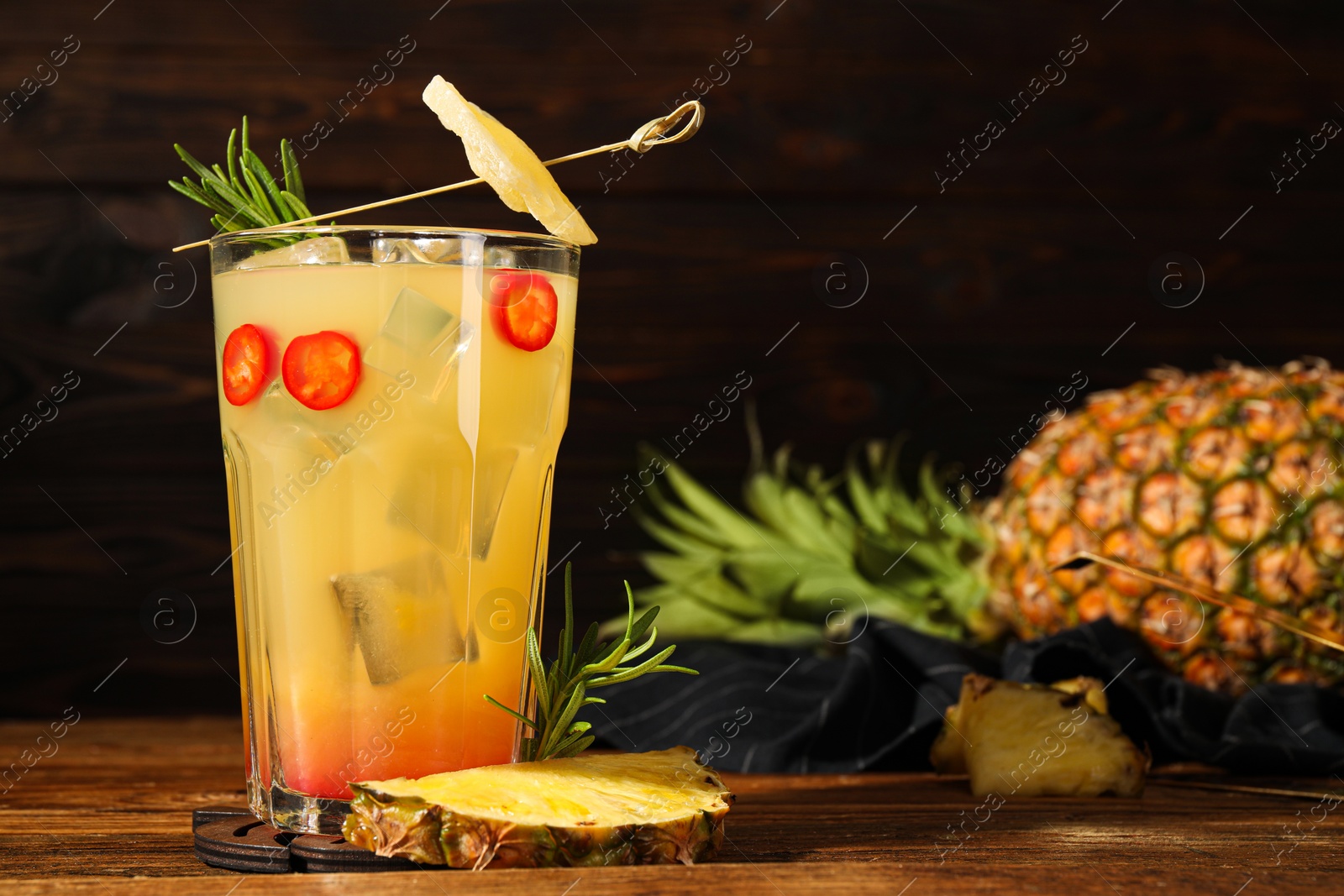 Photo of Spicy pineapple cocktail with chili pepper, rosemary and fresh fruit on wooden table. Space for text