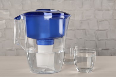 Filter jug and glass with purified water on white table indoors