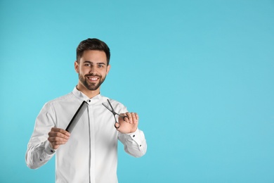 Young hairstylist holding professional scissors and comb on color background, space for text