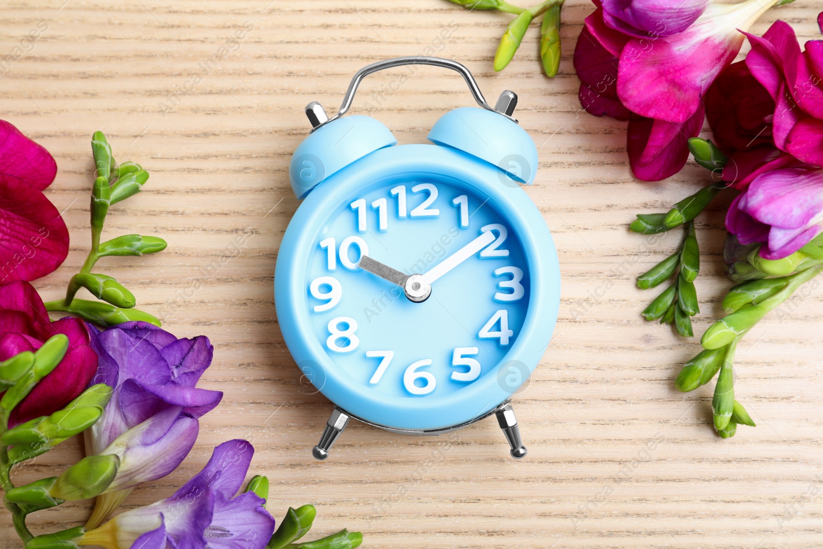 Photo of Light blue alarm clock and spring flowers on wooden table, flat lay. Time change