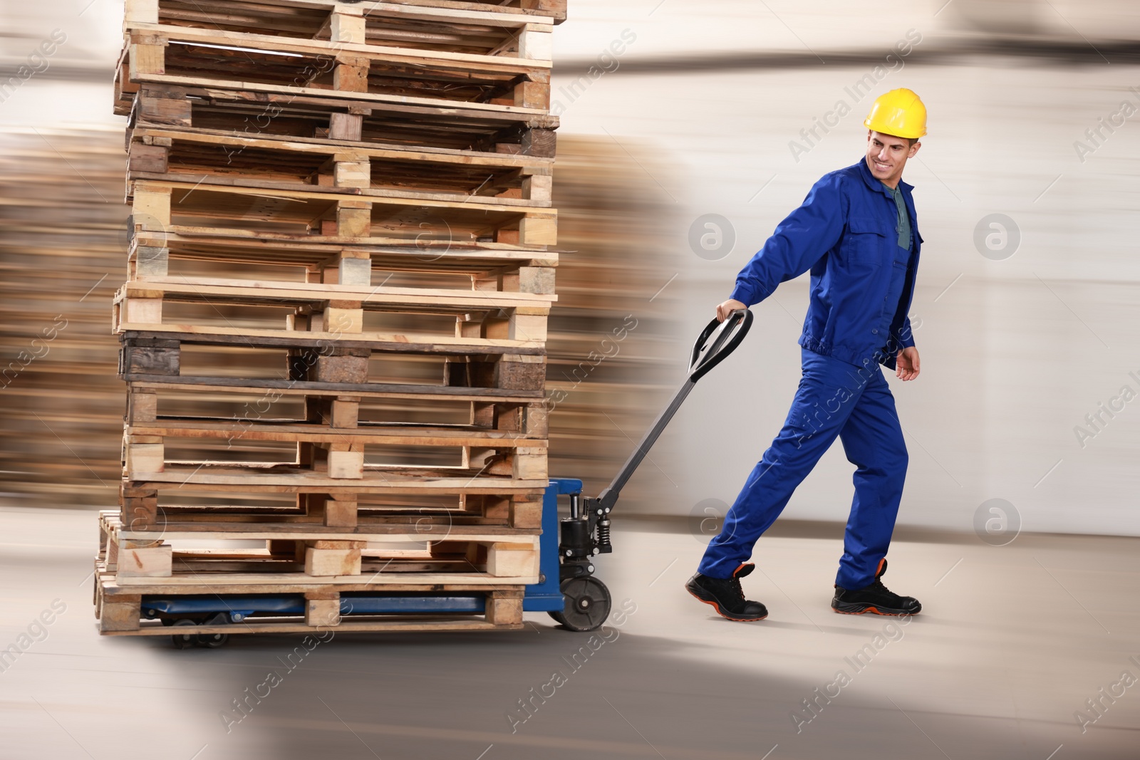 Image of Worker moving wooden pallets with manual forklift in warehouse