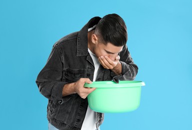 Man with basin suffering from nausea on light blue background. Food poisoning