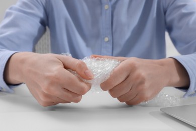 Photo of Woman popping bubble wrap at table in office, closeup. Stress relief