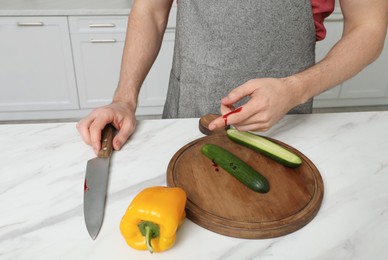 Man cut finger with knife while cooking at white marble table in kitchen, closeup