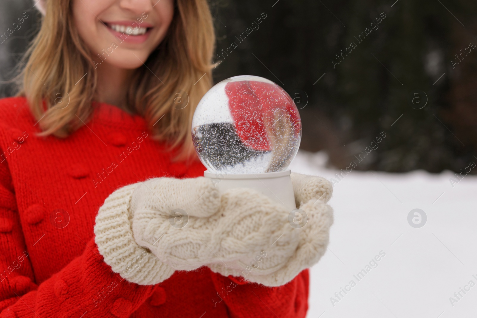 Photo of Woman with knitted mittens holding snow globe outdoors, closeup. Space for text