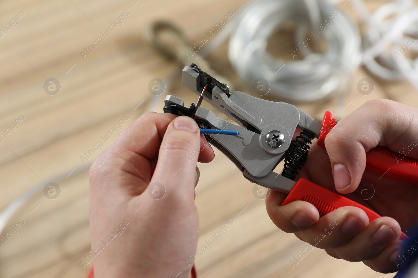 Photo of Professional electrician stripping wiring at wooden table, above view