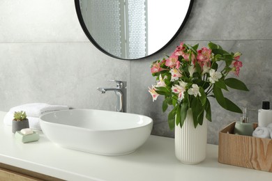 Photo of Vase with beautiful Alstroemeria flowers and toiletries near sink in bathroom