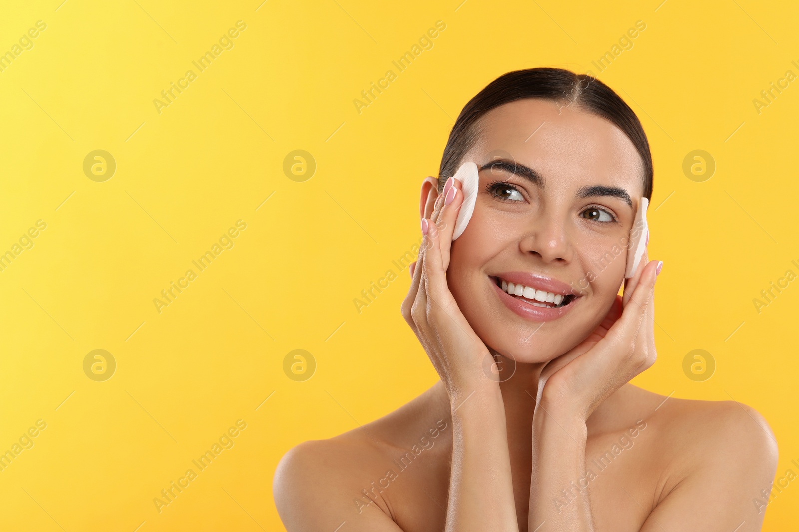 Photo of Beautiful woman removing makeup with cotton pads on yellow background. Space for text