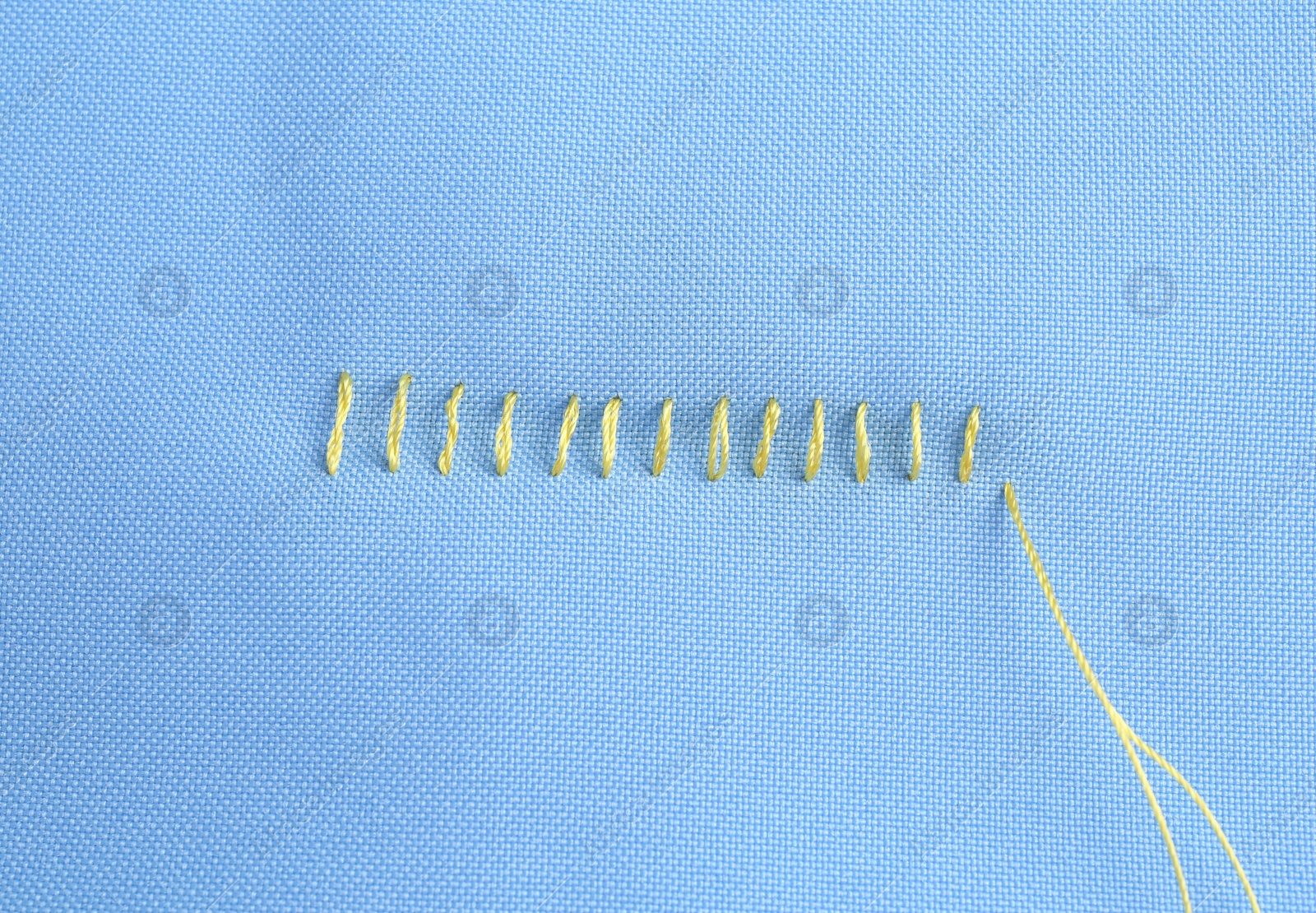 Photo of Sewing thread and stitches on light blue cloth, top view