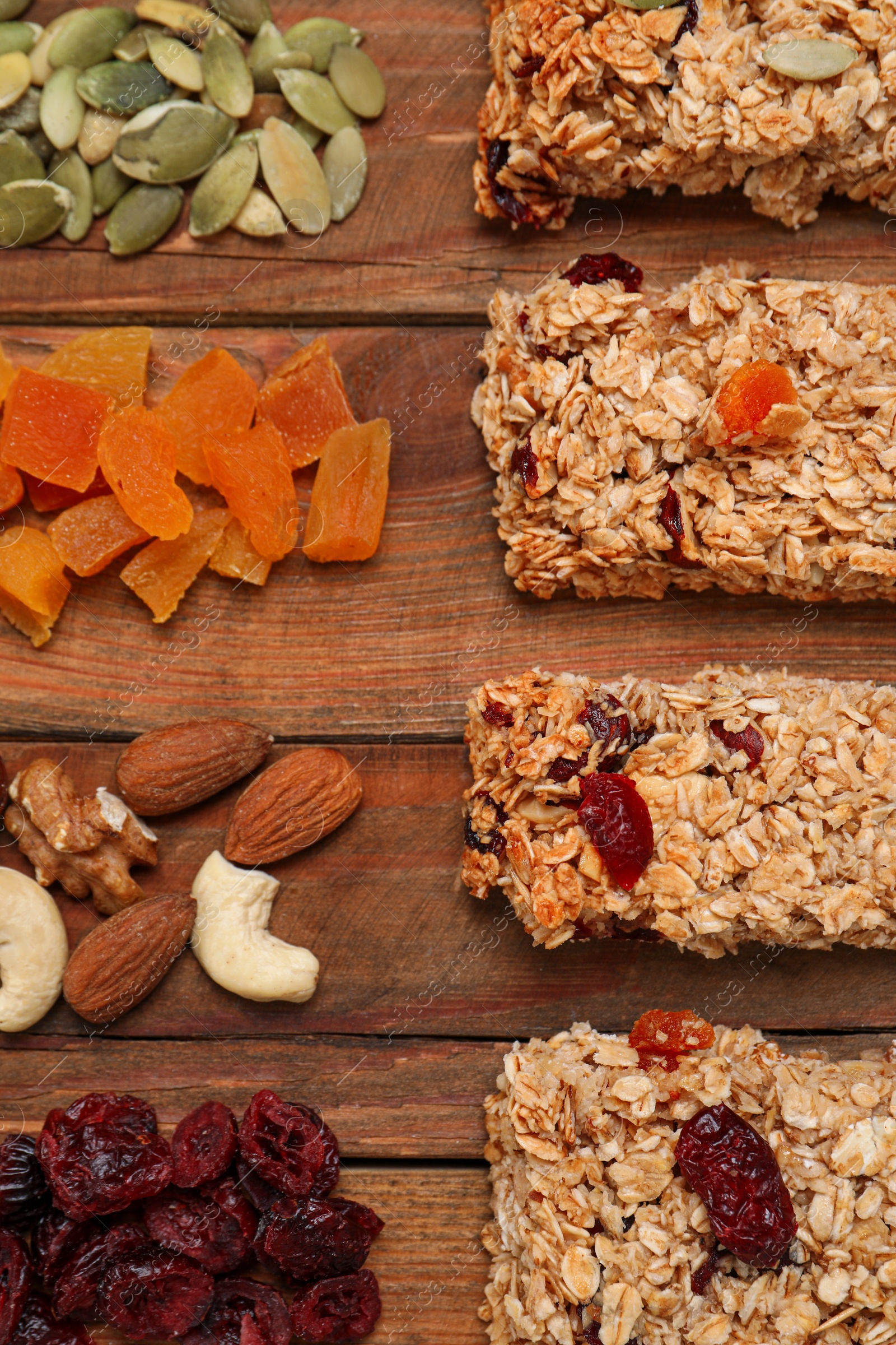 Photo of Different tasty granola bars and ingredients on wooden table, flat lay