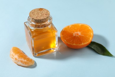 Aromatic tangerine essential oil in bottle and citrus fruit on light blue table