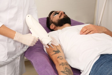 Photo of Young man undergoing laser tattoo removal procedure in salon