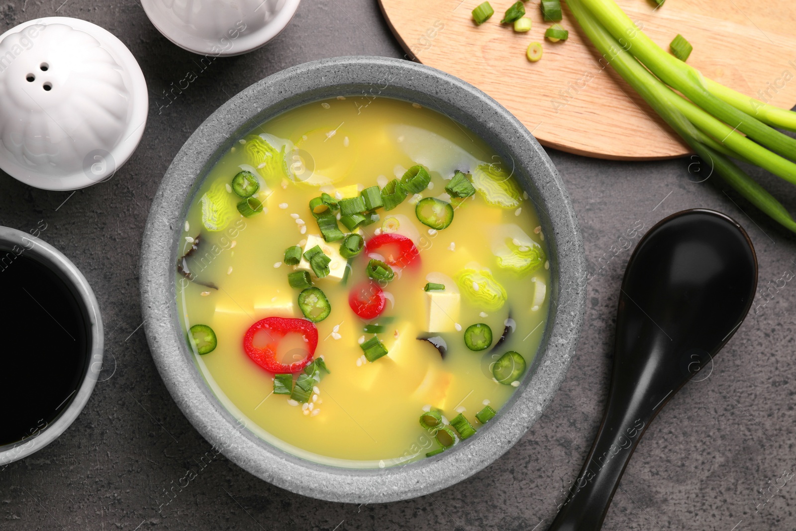 Photo of Bowl of delicious miso soup with tofu served on grey table, flat lay