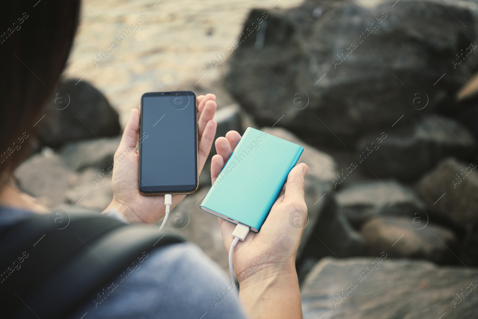 Photo of Woman charging smartphone with power bank on rocky mountain, closeup