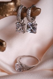 Photo of Elegant jewelry. Stylish presentation of luxury earrings and ring on pink cloth, closeup