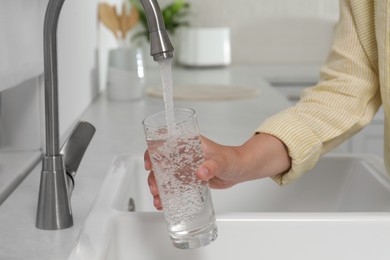 Woman filling glass with water from tap in kitchen, closeup