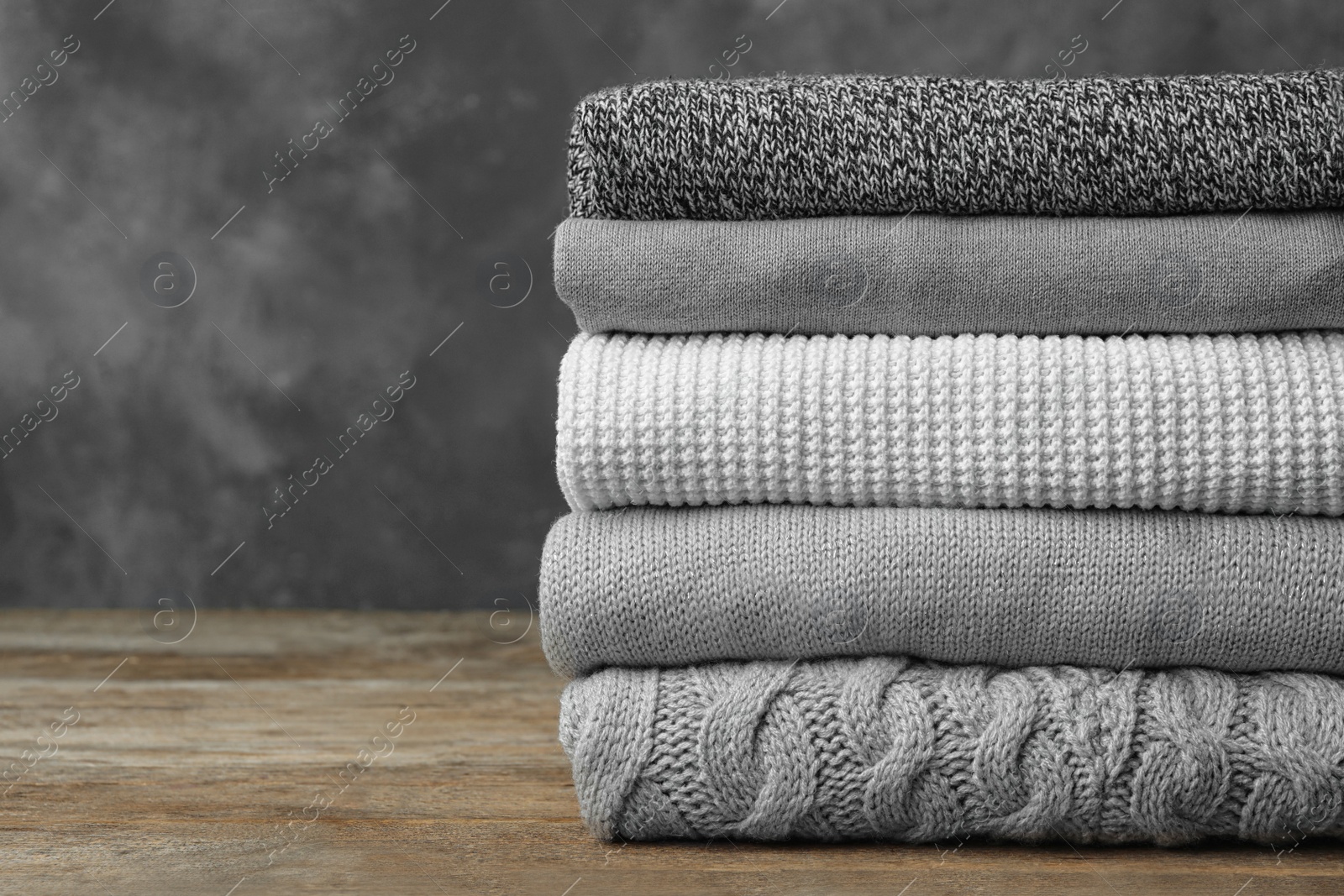 Photo of Stack of warm clothes on wooden table against grey background. Autumn season