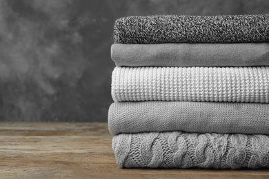 Photo of Stack of warm clothes on wooden table against grey background. Autumn season