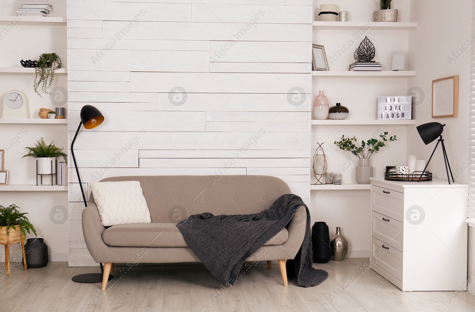 Photo of Stylish living room interior with comfortable sofa, wall shelves and beautiful decor elements