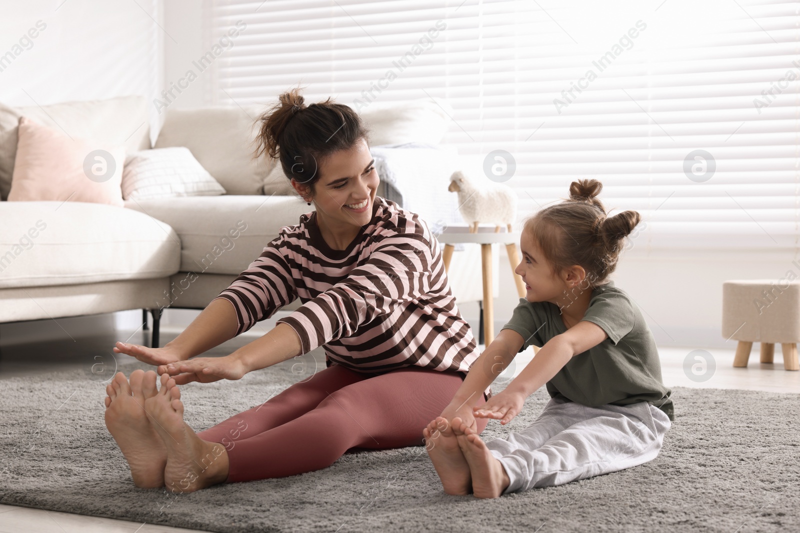 Photo of Young mother and her daughter stretching together at home