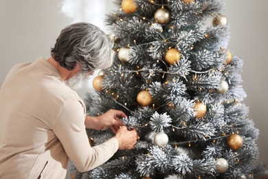 Mature man decorating Christmas tree at home