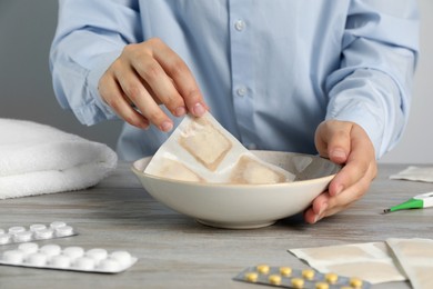 Woman dipping mustard plaster into bowl with water at wooden table, closeup