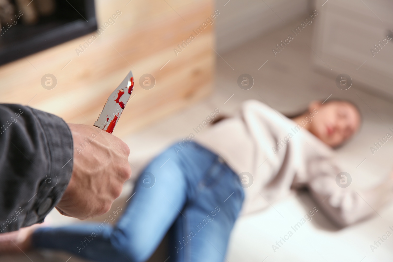 Photo of Man with bloody knife and his victim on floor indoors, closeup. Dangerous criminal