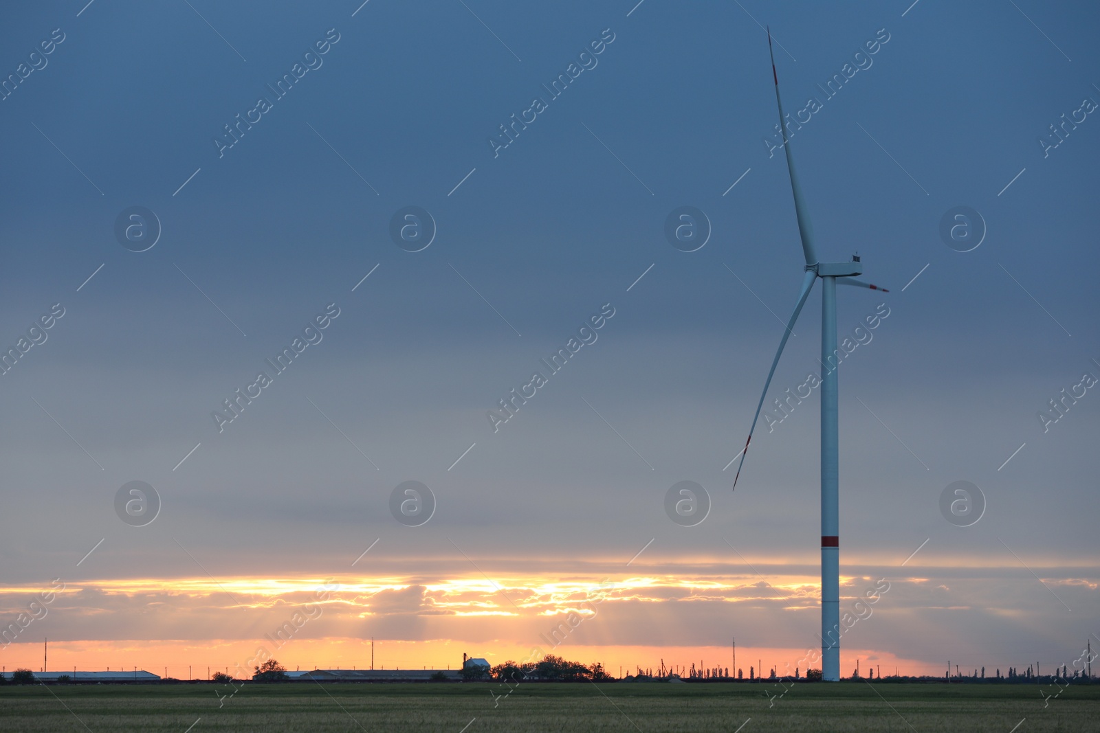 Photo of Beautiful view of field with wind turbine at sunset. Alternative energy source