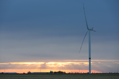 Beautiful view of field with wind turbine at sunset. Alternative energy source