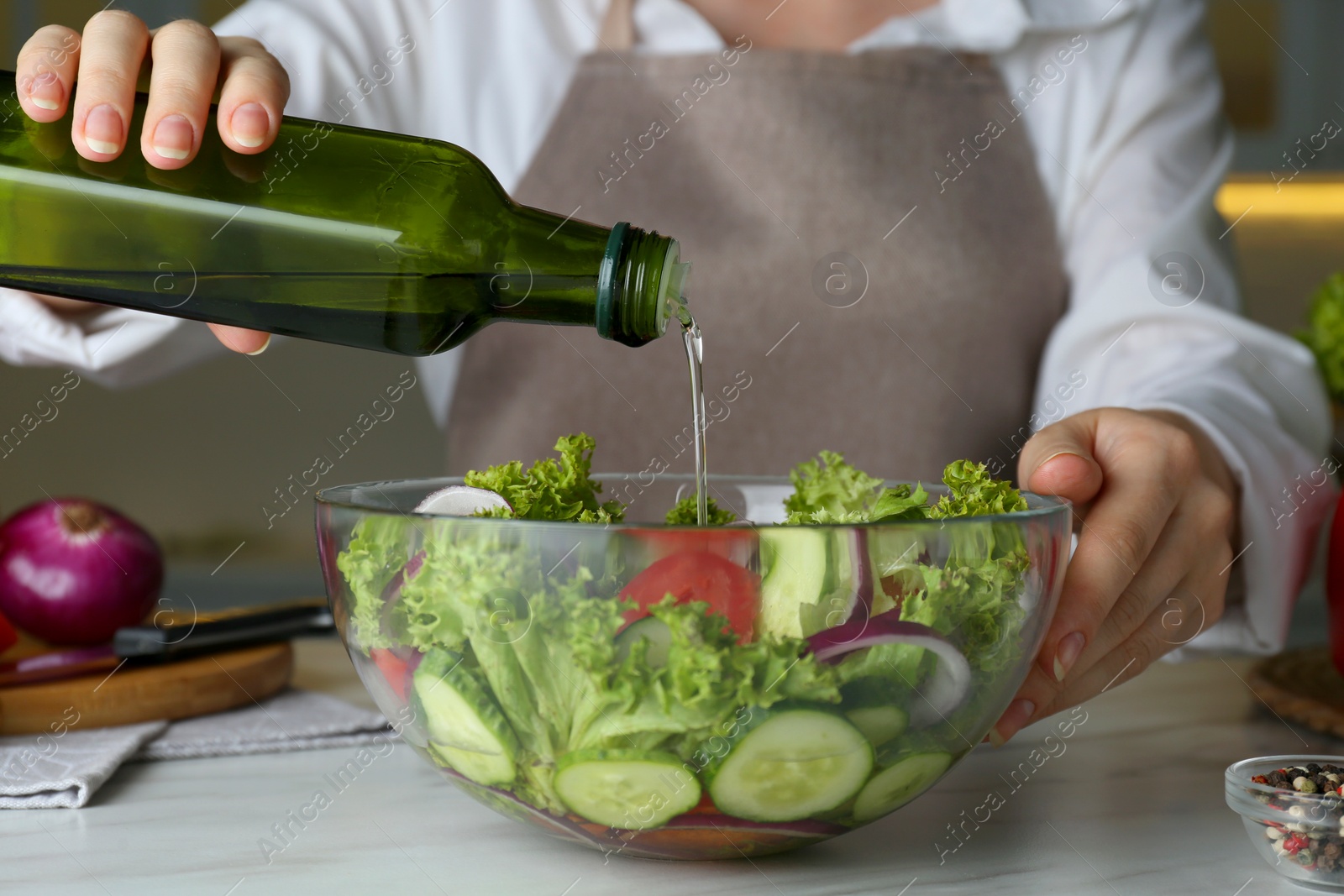 Photo of Woman adding cooking oil to delicious salad at table, closeup