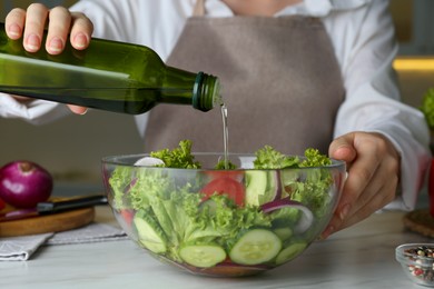 Woman adding cooking oil to delicious salad at table, closeup