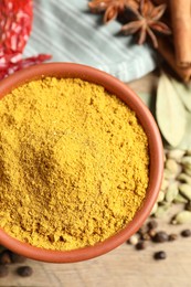 Photo of Curry powder in bowl and other spices on wooden table, top view
