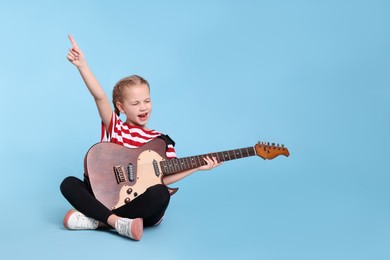 Cute girl with electric guitar on light blue background
