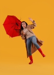 Emotional woman with umbrella caught in gust of wind on yellow background