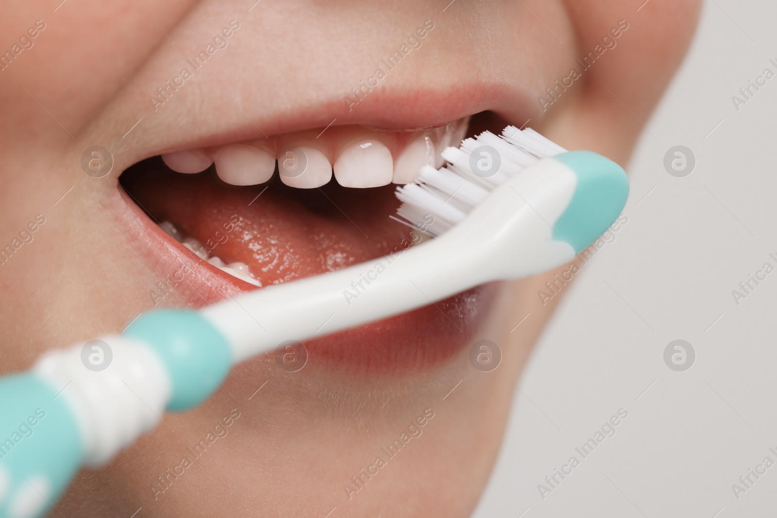 Photo of Cute little boy brushing his teeth with plastic toothbrush on light grey background, closeup