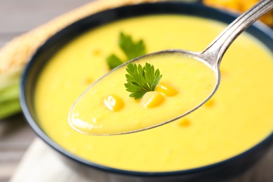 Photo of Spoon of delicious creamy corn soup over bowl, closeup