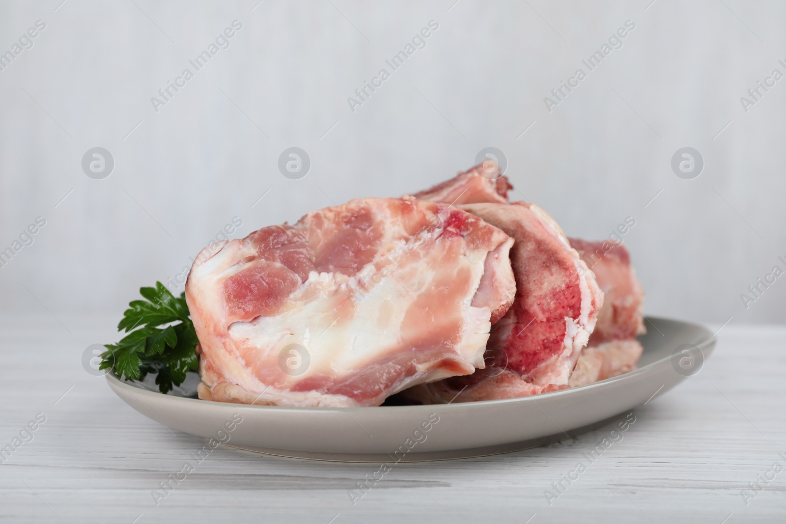 Photo of Plate with raw chopped meaty bones and parsley on white wooden table