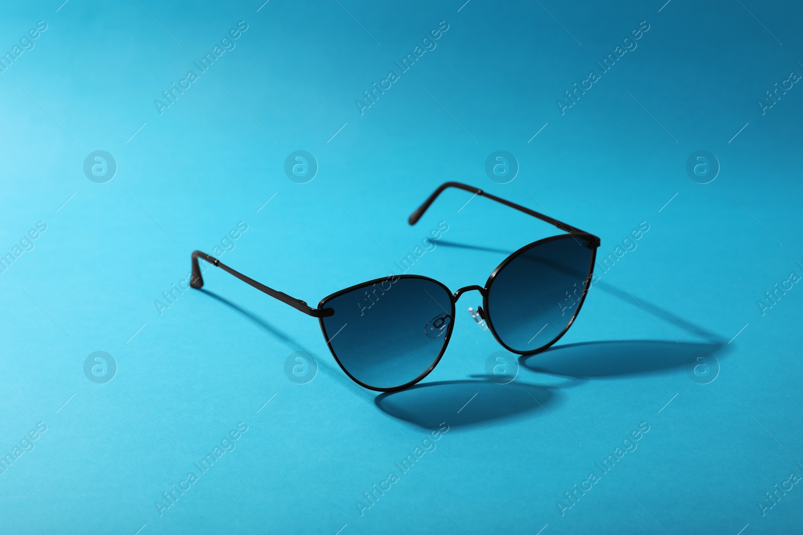 Photo of Sunglasses on light blue background. Stylish accessory